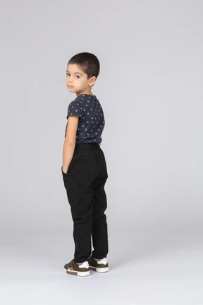 Side view of a cute boy in casual clothes posing with hands in pockets