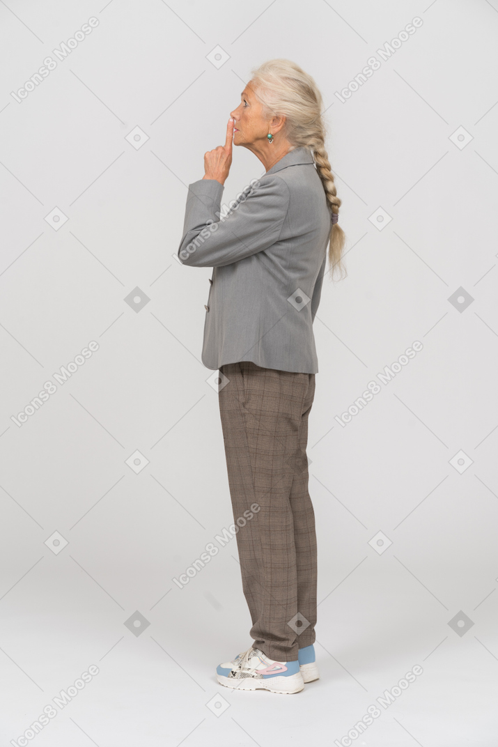 Vista lateral de uma senhora idosa de terno fazendo um gesto de shh