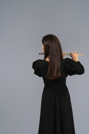 Schwarze ansicht einer jungen dame im schwarzen kleid, die flöte spielt