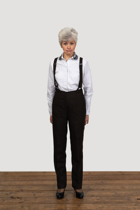 Front view of an old displeased female in office clothes grimacing with her hands behind back