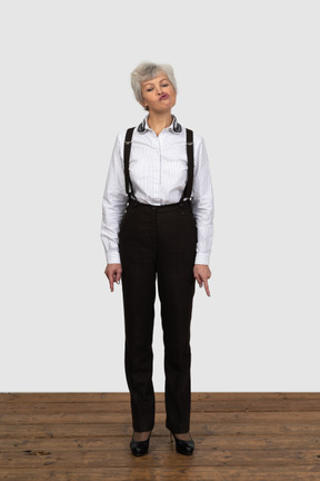 Vorderansicht einer alten grimassenfrau in bürokleidung, die nach unten zeigt