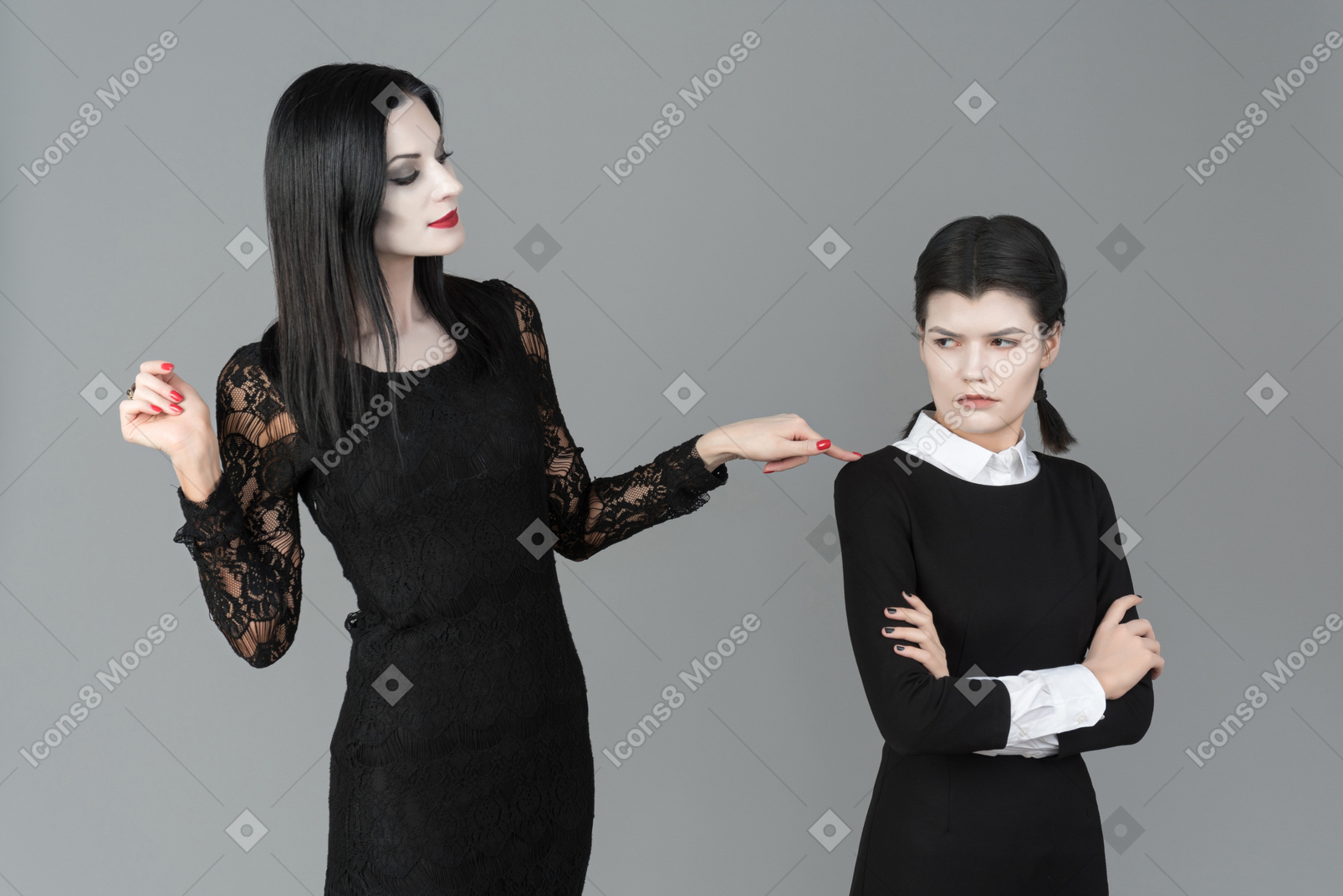Morticia addams looking at wednesday which is standing with her hands folded