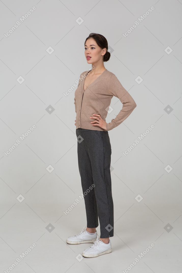Vue de trois quarts d'une jeune femme en pull et pantalon mettant les mains sur les hanches