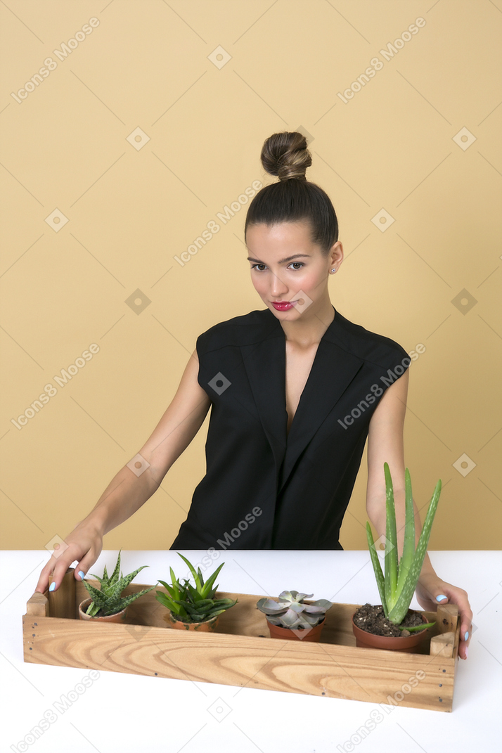 Young beautiful woman sitting next to a wooden box with some home plants in it