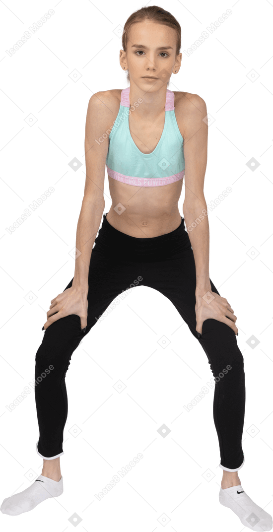 Vue de face d'une adolescente en tenue de sport accroupie et mettant les mains sur les hanches