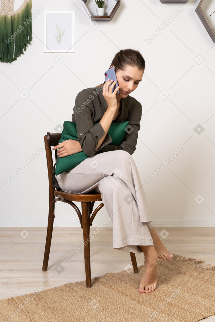 Front view of a young woman sitting on a chair while having a phone call