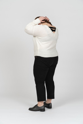 Mulher gorducha em suéter branco em pé com as mãos atrás da cabeça