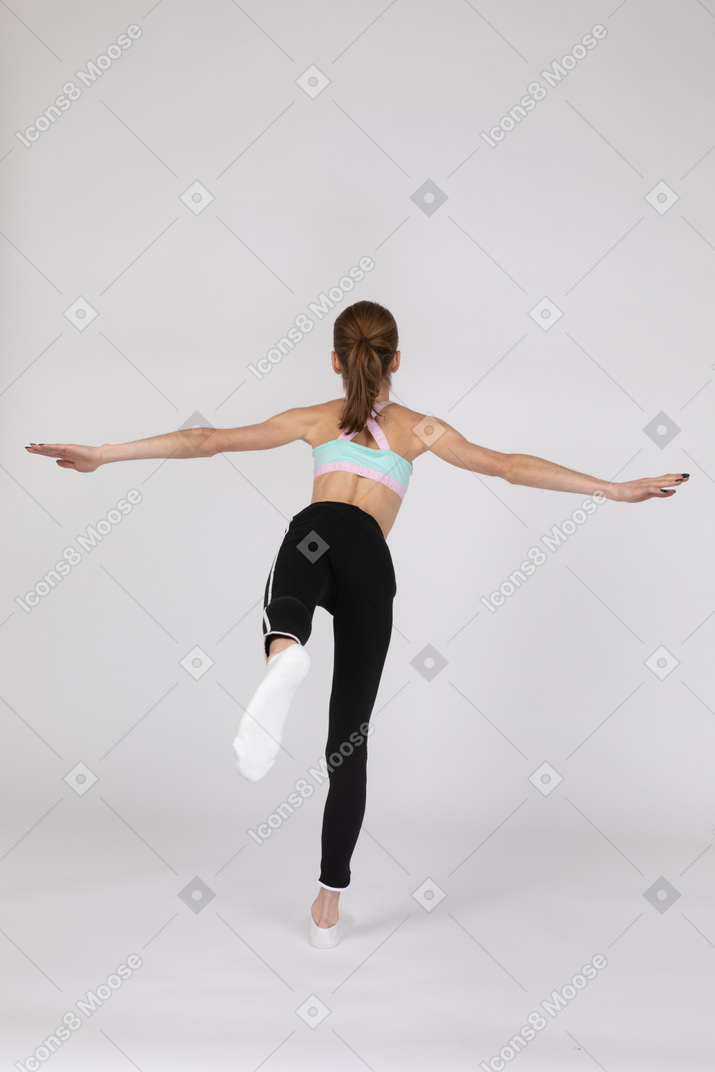 Vista posterior de una jovencita en ropa deportiva en equilibrio sobre su pierna