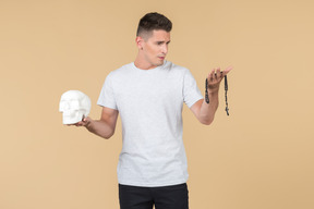 Young guy holding skull in one hand and looking at prayer beads he's holding in another hand