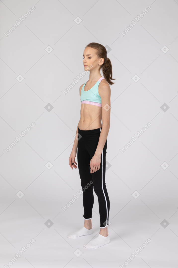 Vista de tres cuartos de una jovencita en ropa deportiva de pie y mirando a un lado