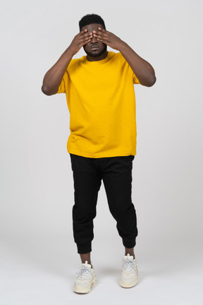 Vorderansicht eines jungen dunkelhäutigen mannes in gelbem t-shirt, der seine augen versteckt