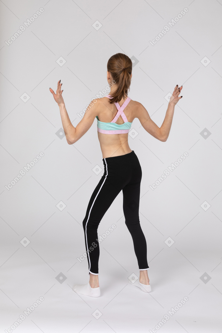 Vista traseira de uma adolescente em roupas esportivas, levantando as mãos e dançando