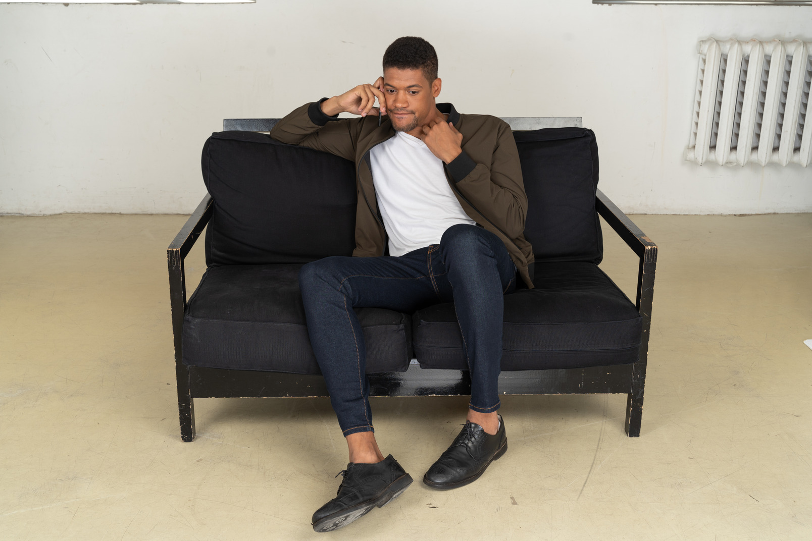 Front view of a perplexed young man sitting on a sofa