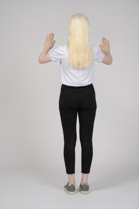 Vista traseira de uma jovem de pé com as duas mãos para cima