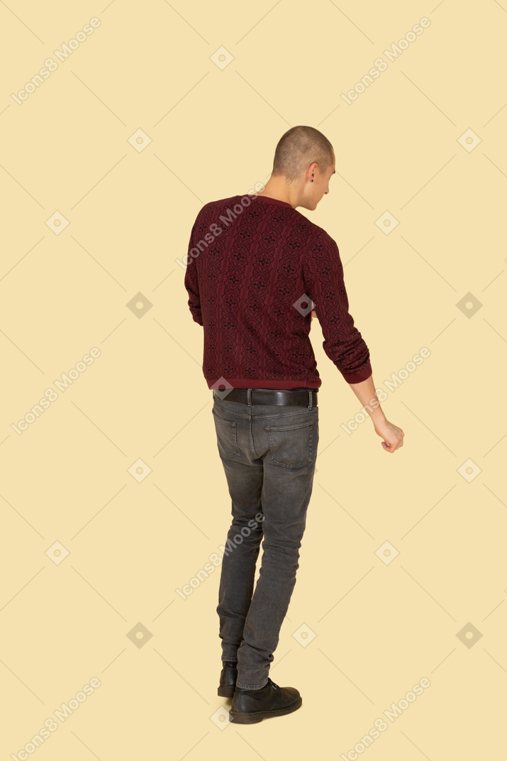 Вид сзади идущего молодого человека в красном пуловере