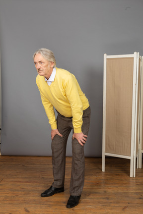 Three-quarter view of an old man leaning forward while putting hands on legs