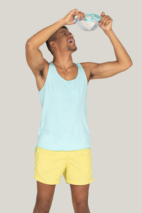 Man in blue tank top and yellow shorts putting on swim mask