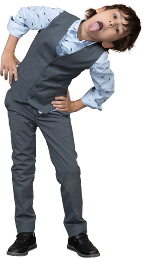 Vue de face d'un garçon en costume gris posant avec les mains sur les hanches et montrant la langue