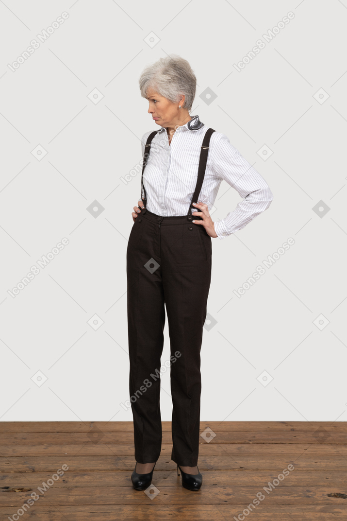 Vue de face d'une vieille dame boudeuse en vêtements de bureau mettant les mains sur les hanches
