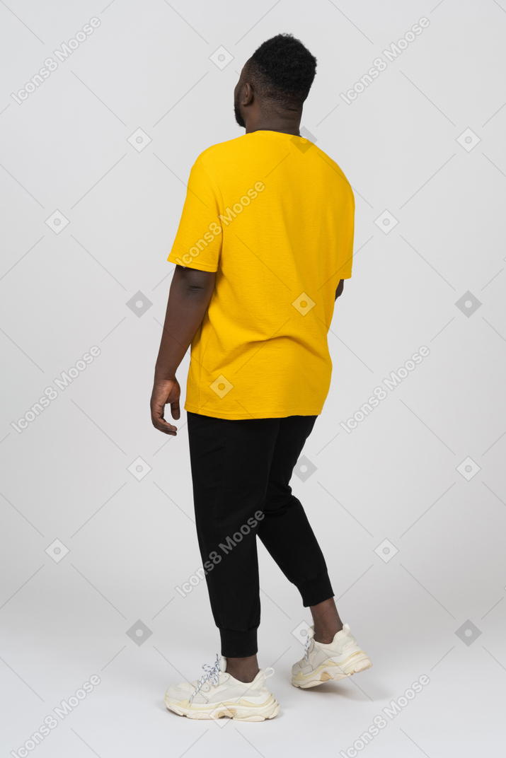Dreiviertelansicht von hinten auf einen jungen dunkelhäutigen mann in gelbem t-shirt, der still steht
