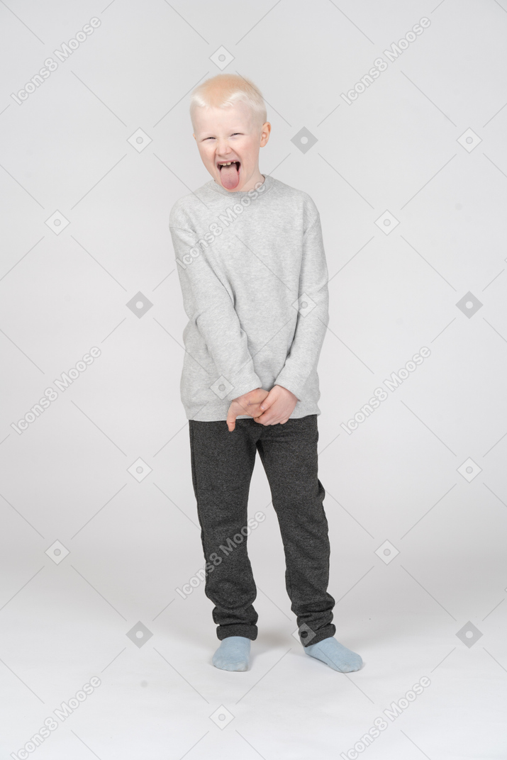 Vista frontal de un niño chico haciendo muecas y mostrando la lengua