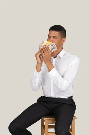 Man in white shirt and black pants sitting on a stool and holding money