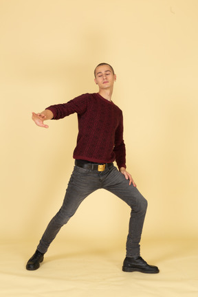 Front view of a young unwilling man in red pullover outstretching his hand