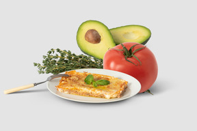 Slice of lasagna on plate next to tomato and avocado