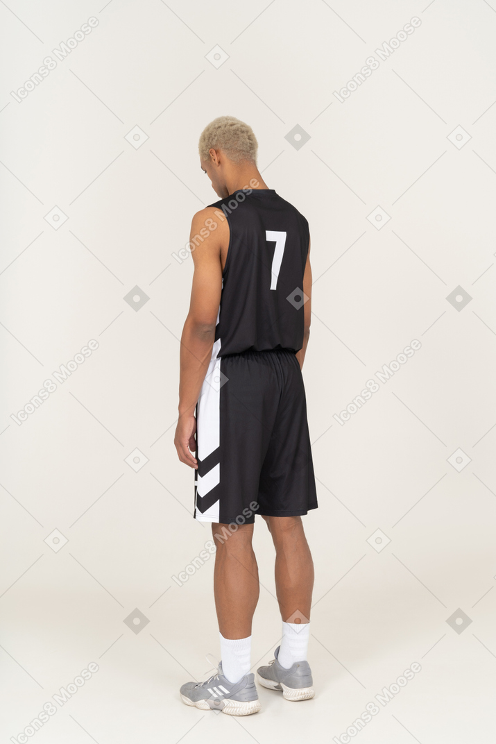 Dreiviertelansicht eines jungen männlichen basketballspielers, der still steht und nach unten schaut