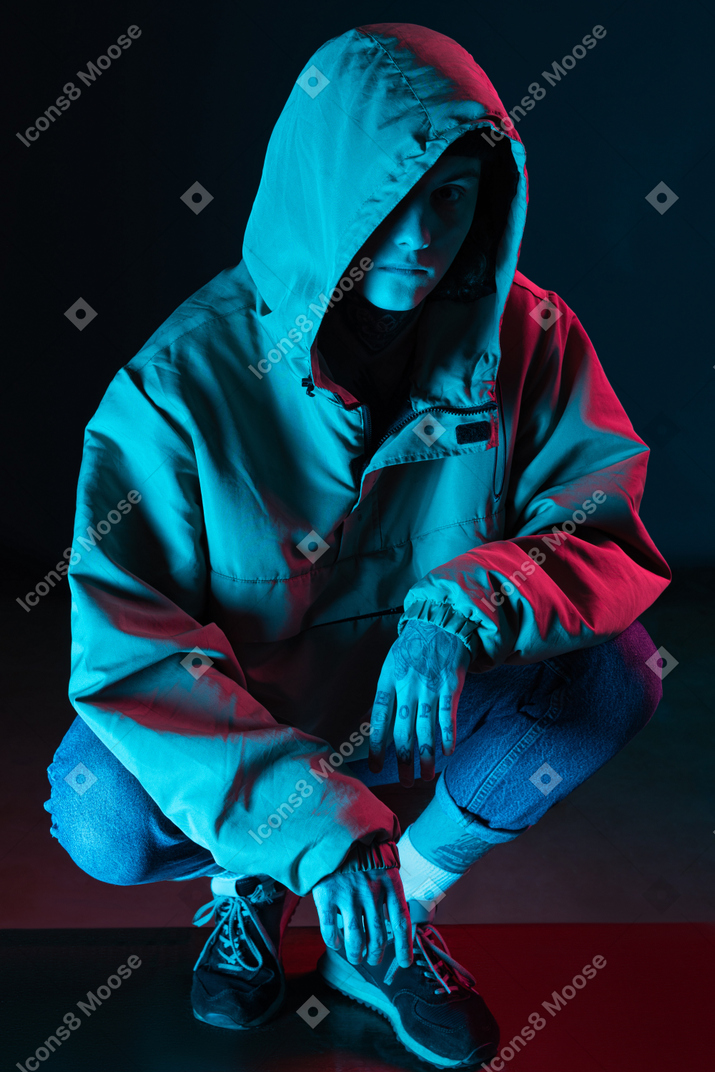 Male model in hoodie sits under blue light