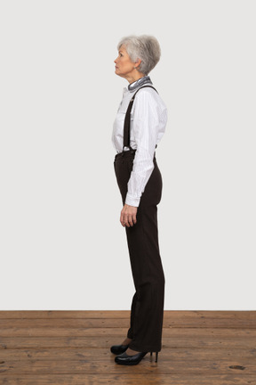 Side view of an old female in office clothes standing still in the room
