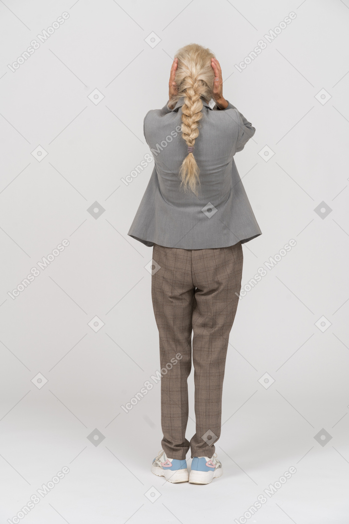 Vista trasera de una anciana en traje cubriendo las orejas con las manos