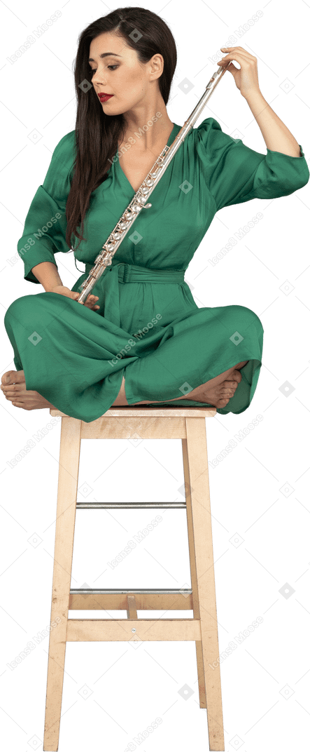 Longitud total de una señorita mirando el clarinete sentado con las piernas cruzadas en una silla de madera