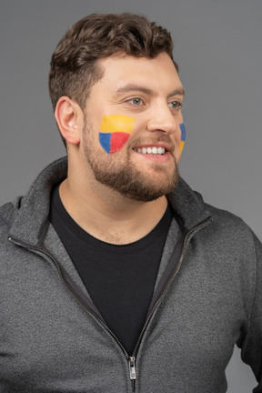 Vista de tres cuartos de un sonriente fanático del fútbol masculino con colorido arte facial