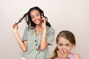 Mulher atraente, falando ao telefone e menina envergonhada com o que ela ouve