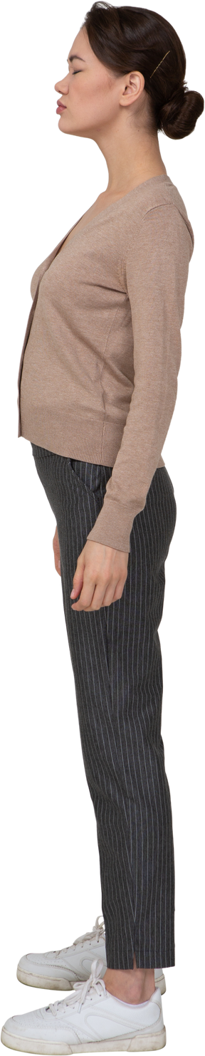 Vista laterale di una giovane donna in pullover e pantaloni in piedi con gli occhi chiusi