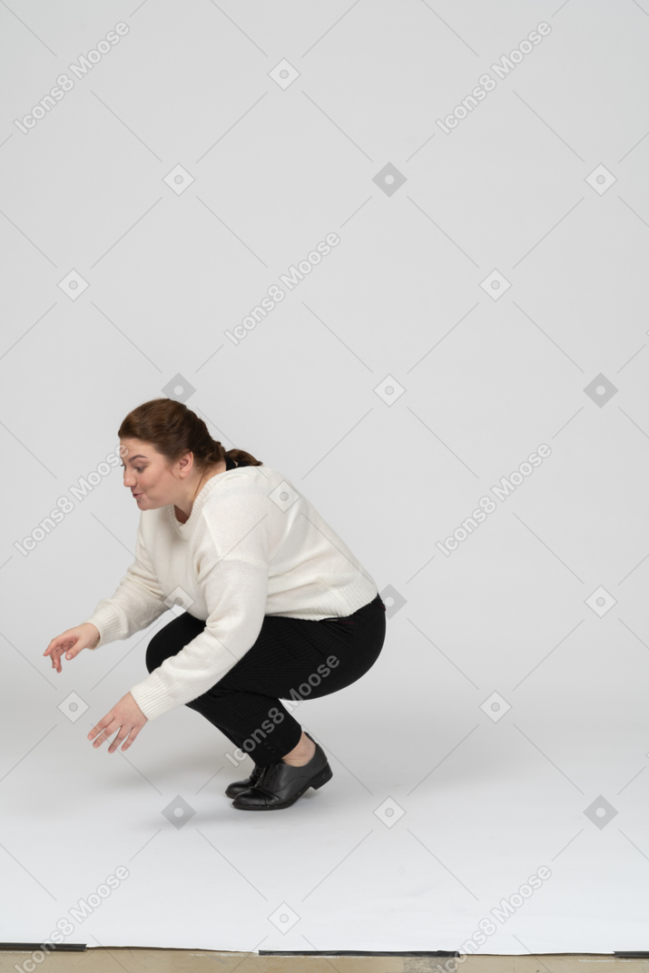 Пухлая женщина в повседневной одежде сидит на корточках, вид сбоку