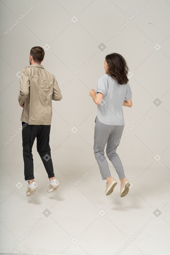 Three quarter back view of young man and woman jumping