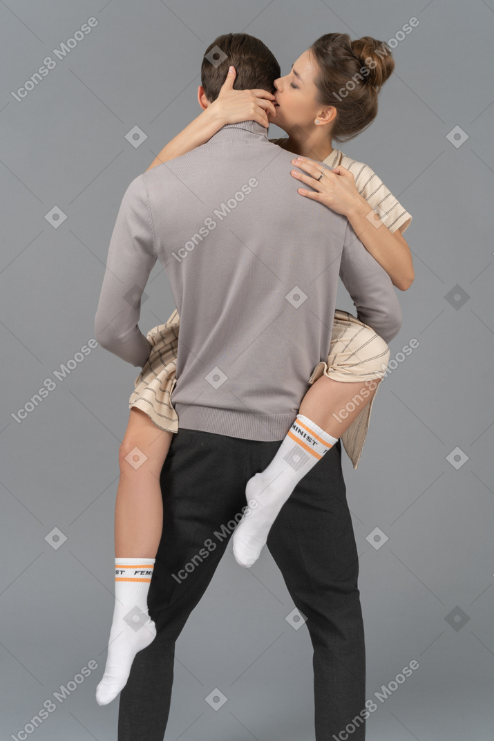 Vista traseira de um jovem segurando sua namorada acima do chão