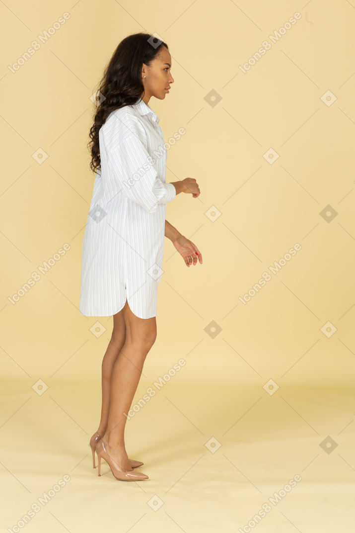 Vista lateral de una mujer joven de piel oscura con vestido blanco