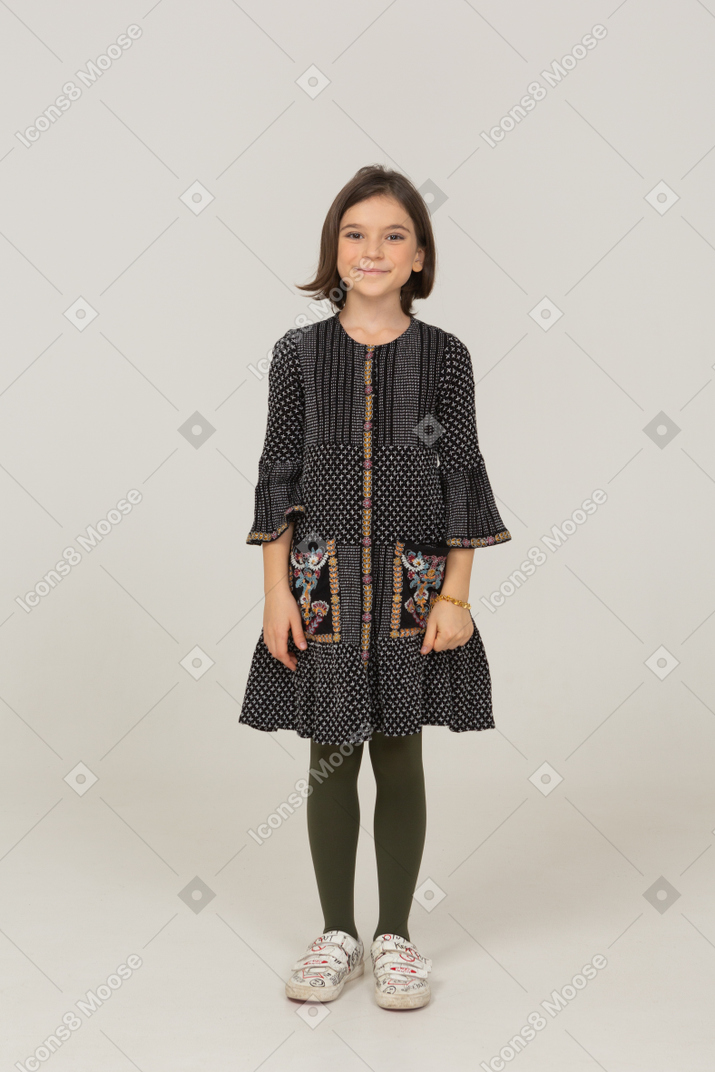 Вид спереди веселой маленькой девочки в платье, смотрящей в камеру