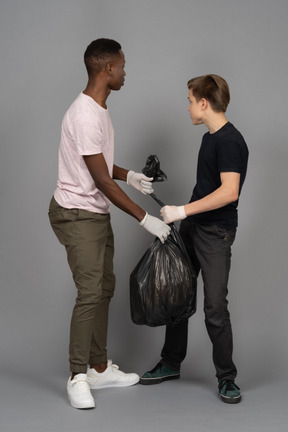 Zwei junge mann, die einen schwarzen müllsack halten