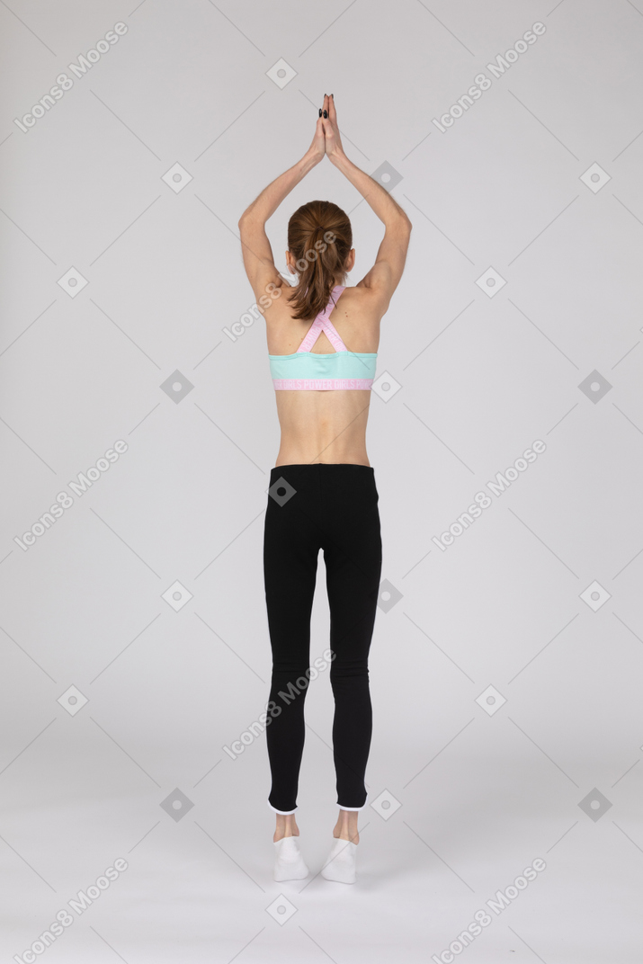 Back view of a teen girl in sportswear standing on tiptoes and raising hands