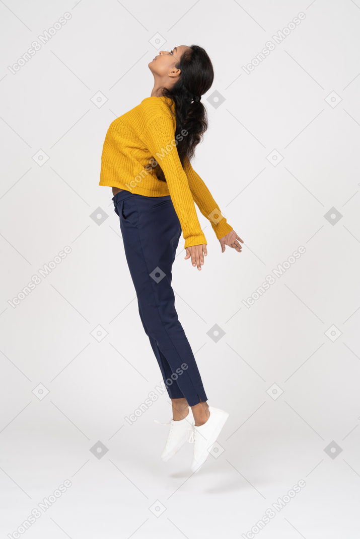 Vista laterale di una ragazza in abiti casual che salta con le braccia tese