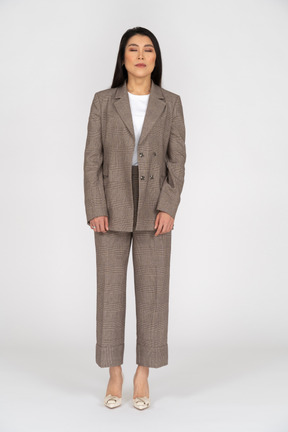 Front view of a young lady in brown business suit standing with her eyes closed