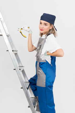 Female worker standing on stepladder and holding pliers