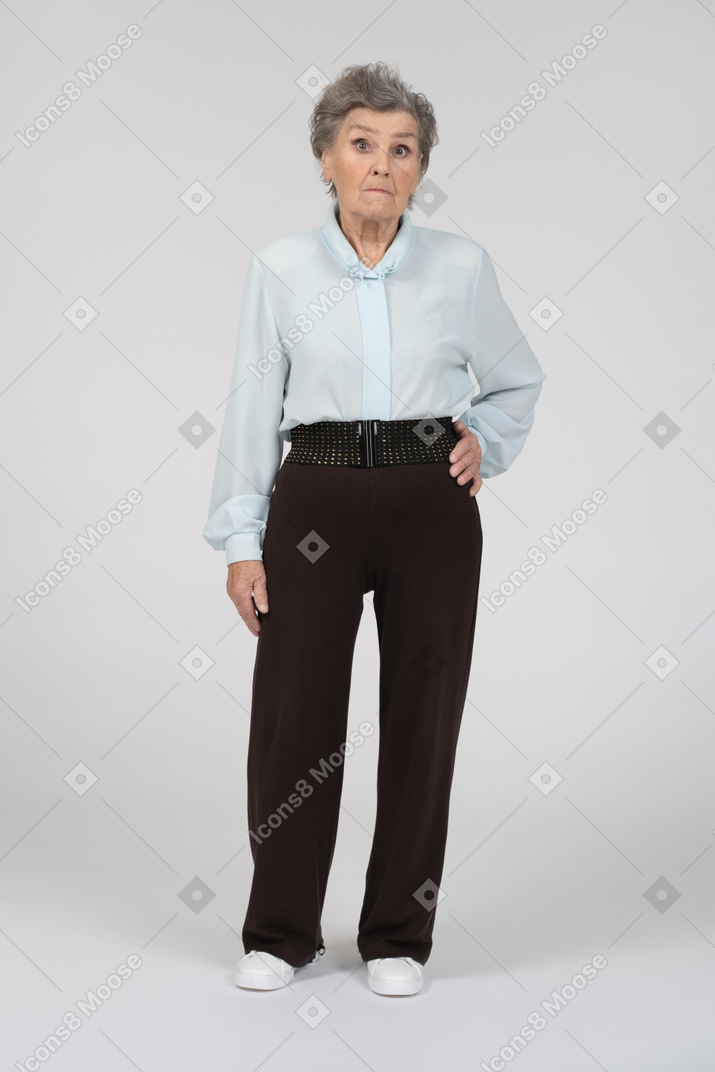 Вид спереди пожилой женщины, выжидающе смотрящей в камеру с рукой на бедре