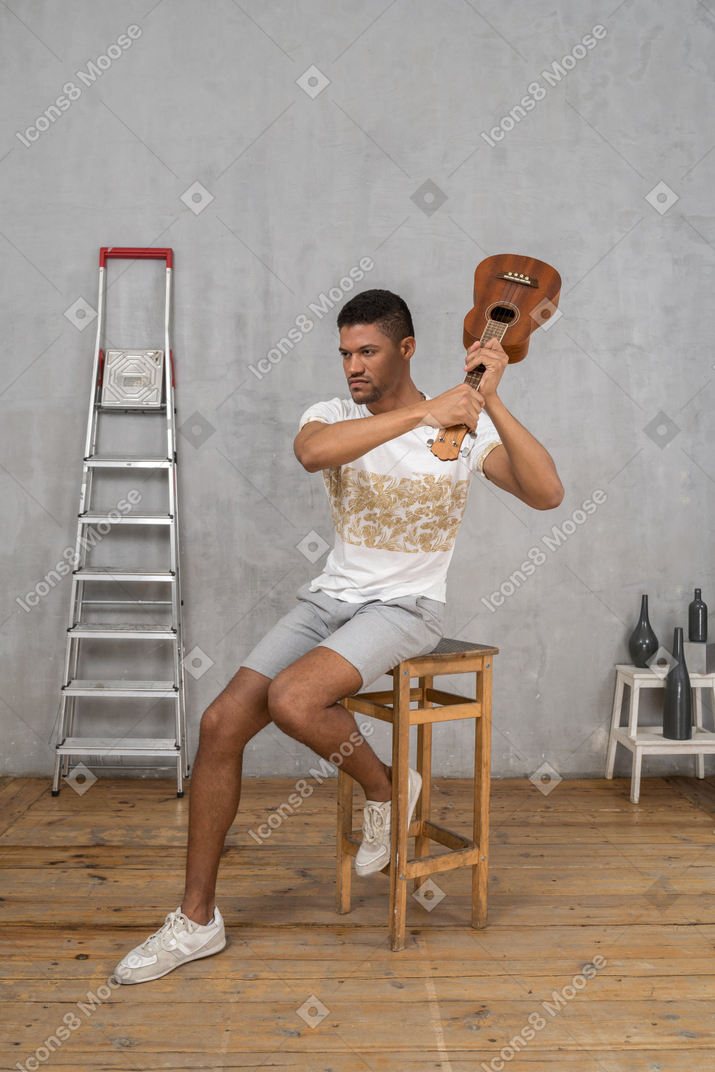 Vista de tres cuartos de un hombre en un taburete balanceando un ukelele tenso