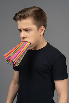 Three-quarter portrait of sad male teenager with plastic straws in mouth