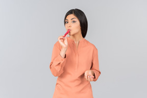 Femme indienne en top orange appliquant un baume à lèvres